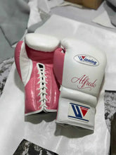 Custom Winning professional lace-up boxing gloves in white leather featuring a vibrant pink leather thumb, pink palm and lace track, official brand patches, and custom red Alfredo script name lettering.