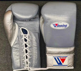 Custom Winning professional lace-up boxing gloves in slate gray leather featuring a metallic silver thumb, metallic silver palm and cuff, official brand patches, and white laces.