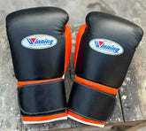 Custom Winning professional hook-and-loop boxing gloves in black leather featuring bright orange thumb linings, orange wrist borders, official white brand patches, and wide velcro straps.