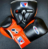 Custom Winning professional boxing sparring set in a matching black and orange premium leather colorway, featuring lace-up training gloves and a face guard headgear with white laces and brand crests.