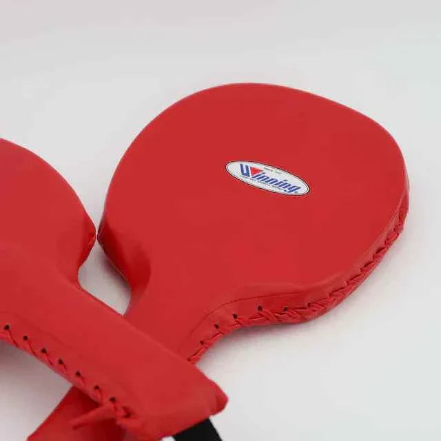 Official Winning professional boxing punch paddles in classic red premium leather showing the outer stitched borders, ergonomic handles, and the iconic brand logo oval crest on the striking surface.