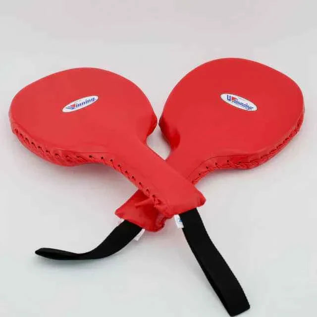 Official Winning professional boxing punch paddles in classic red premium leather showing the outer stitched borders, ergonomic handles, and the iconic brand logo oval crest on the striking surface.