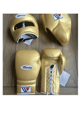 Custom Winning professional 3-piece boxing sparring gear set in a matching shimmering metallic gold premium leather colorway, featuring lace-up training gloves, a face guard headgear, and a groin protector resting on a light wooden surface.