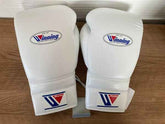Official Winning professional lace-up training boxing gloves in pristine white premium leather resting on a wooden surface, featuring the iconic brand logo oval crest on the knuckle face and cuff patches.