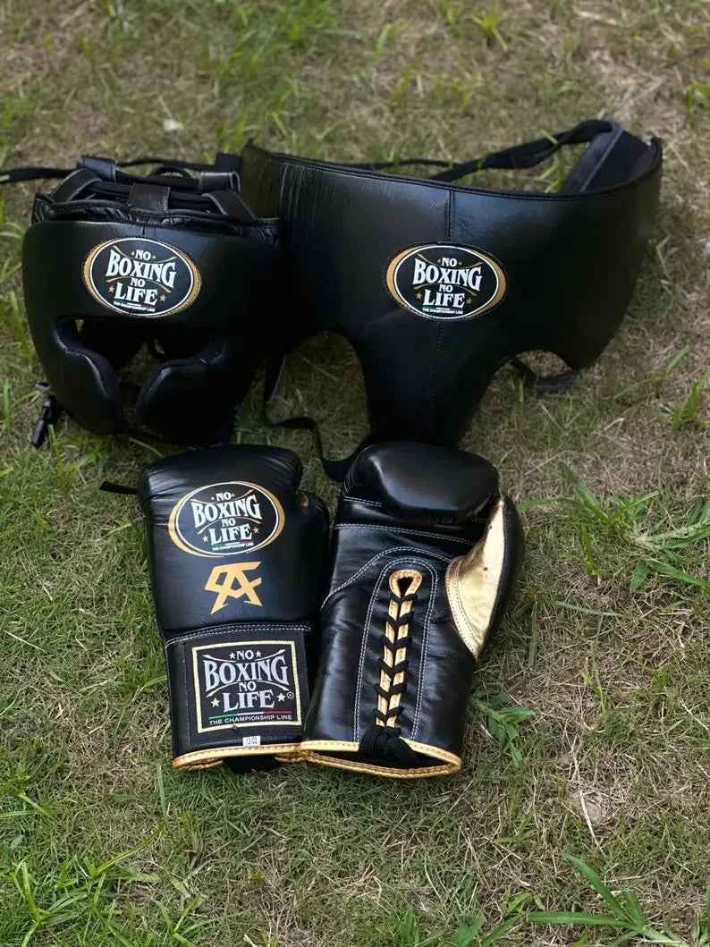 No Boxing No Life professional custom 3-piece boxing sparring gear set featuring matching lace-up gloves with gold CA logo, a cheek headguard, and a groinguard in premium black leather with metallic gold trim accents on grass.