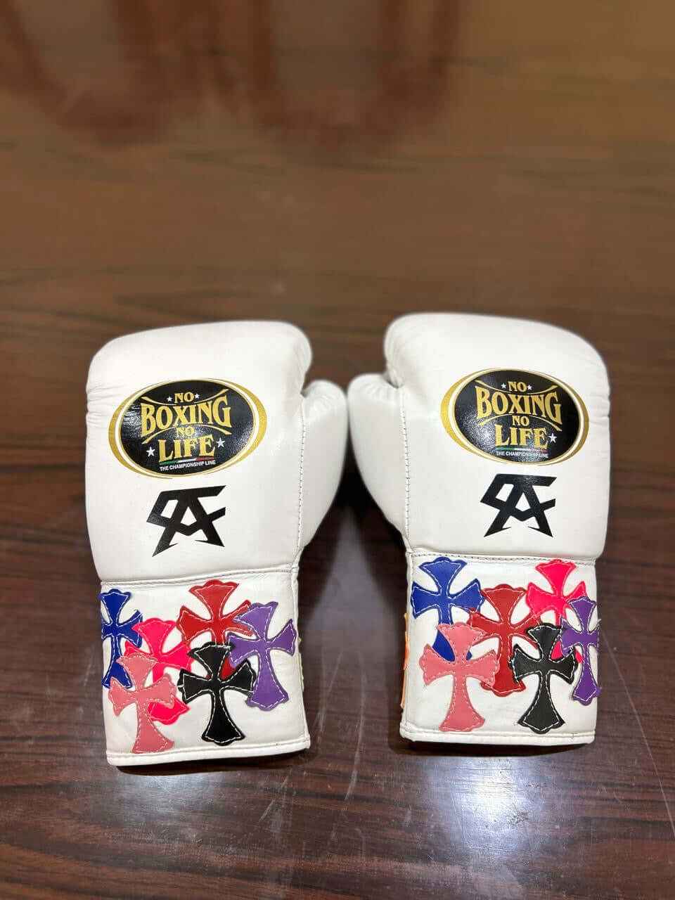 Custom No Boxing No Life professional lace-up boxing gloves in white leather featuring black Canelo Alvarez CA logos and multiple layered multi-color leather cross patches stitched onto the cuffs.