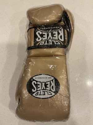 Official Cleto Reyes professional lace-up training boxing gloves in gold metallic leather featuring a high-sheen champagne finish with black printed brand logos, brand new in protective plastic packaging.