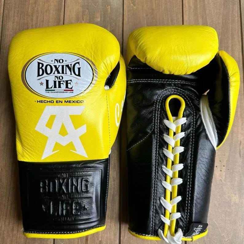 No Boxing No Life professional lace-up boxing gloves in yellow and black leather featuring the official brand patch and Canelo Alvarez CA logo.