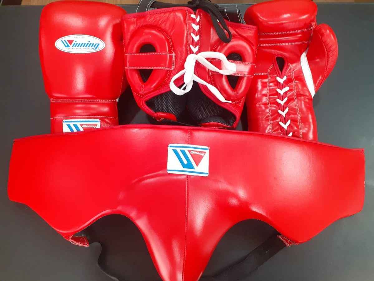 Official Winning professional 3-piece boxing sparring gear set in a matching classic red premium leather colorway, featuring lace-up training gloves, a face guard headgear, and a groin protector grouped together.