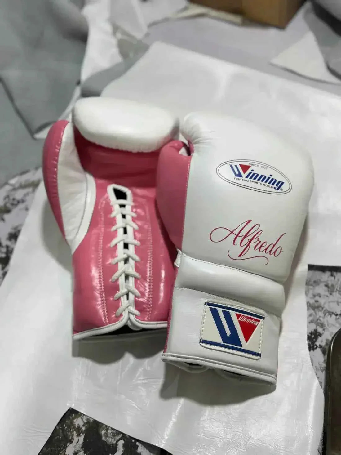 Custom Winning professional lace-up boxing gloves in white leather featuring a vibrant pink leather thumb, pink palm and lace track, official brand patches, and custom red Alfredo script name lettering.