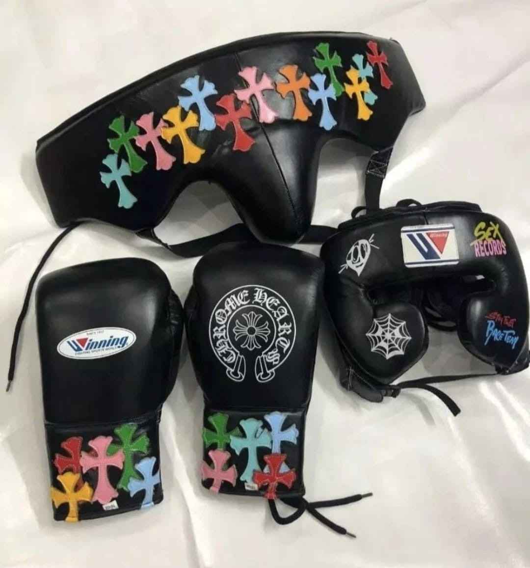 Custom Winning professional 3-piece boxing sparring gear set in black leather featuring multi-colored cemetery cross patches and streetwear graphics across the lace-up gloves, face guard headgear, and groin protector.