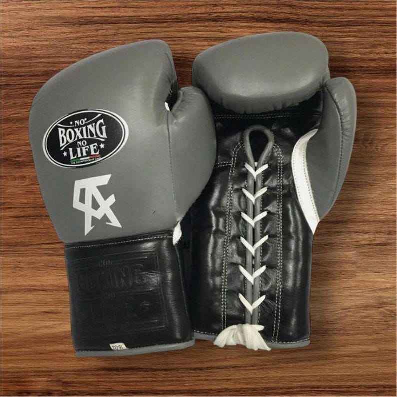Official No Boxing No Life professional lace-up boxing gloves in gray and black leather featuring a white Canelo Alvarez CA logo printed below the black oval brand insignia.