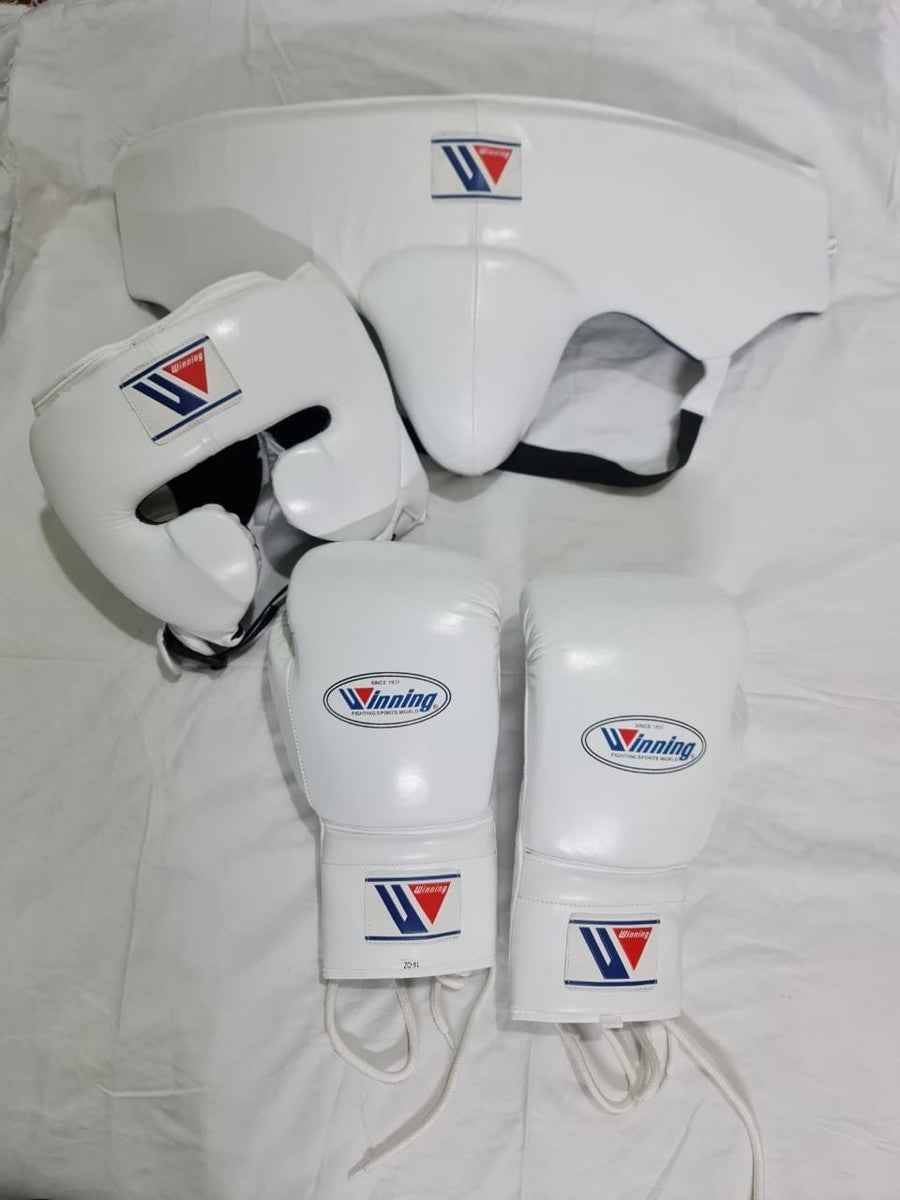 Official Winning professional 3-piece boxing sparring gear set in a matching classic white premium leather colorway, featuring lace-up training gloves, a face guard headgear, and a groin protector grouped together over a white sheet backdrop.