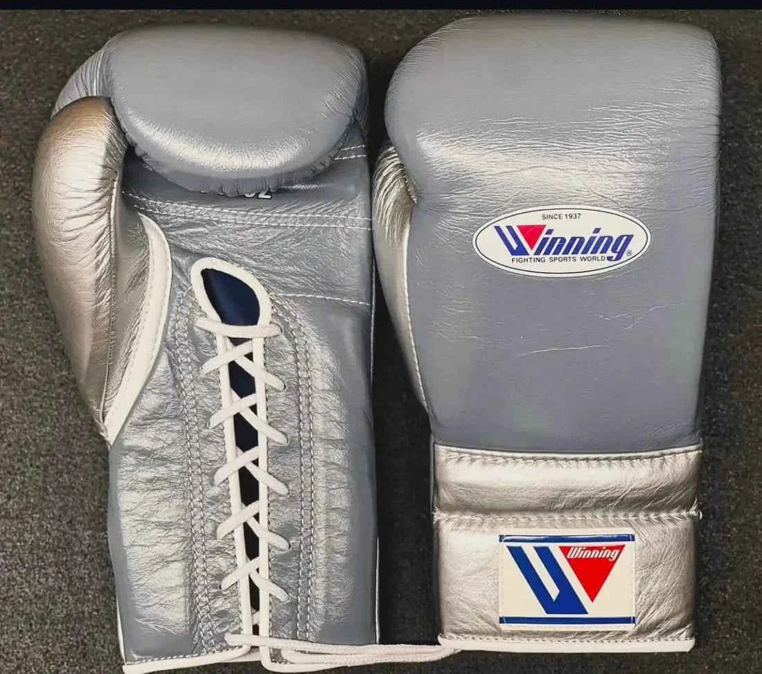 Custom Winning professional lace-up boxing gloves in slate gray leather featuring a metallic silver thumb, metallic silver palm and cuff, official brand patches, and white laces.