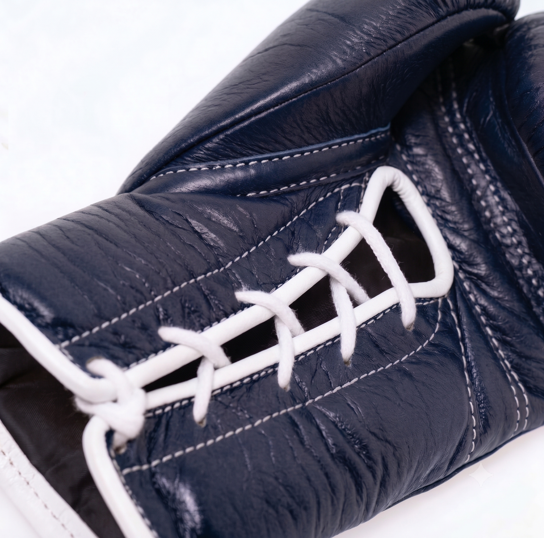 Close-up of a dark navy leather boxing glove with white laces and white contrast stitching, set against a plain white background.