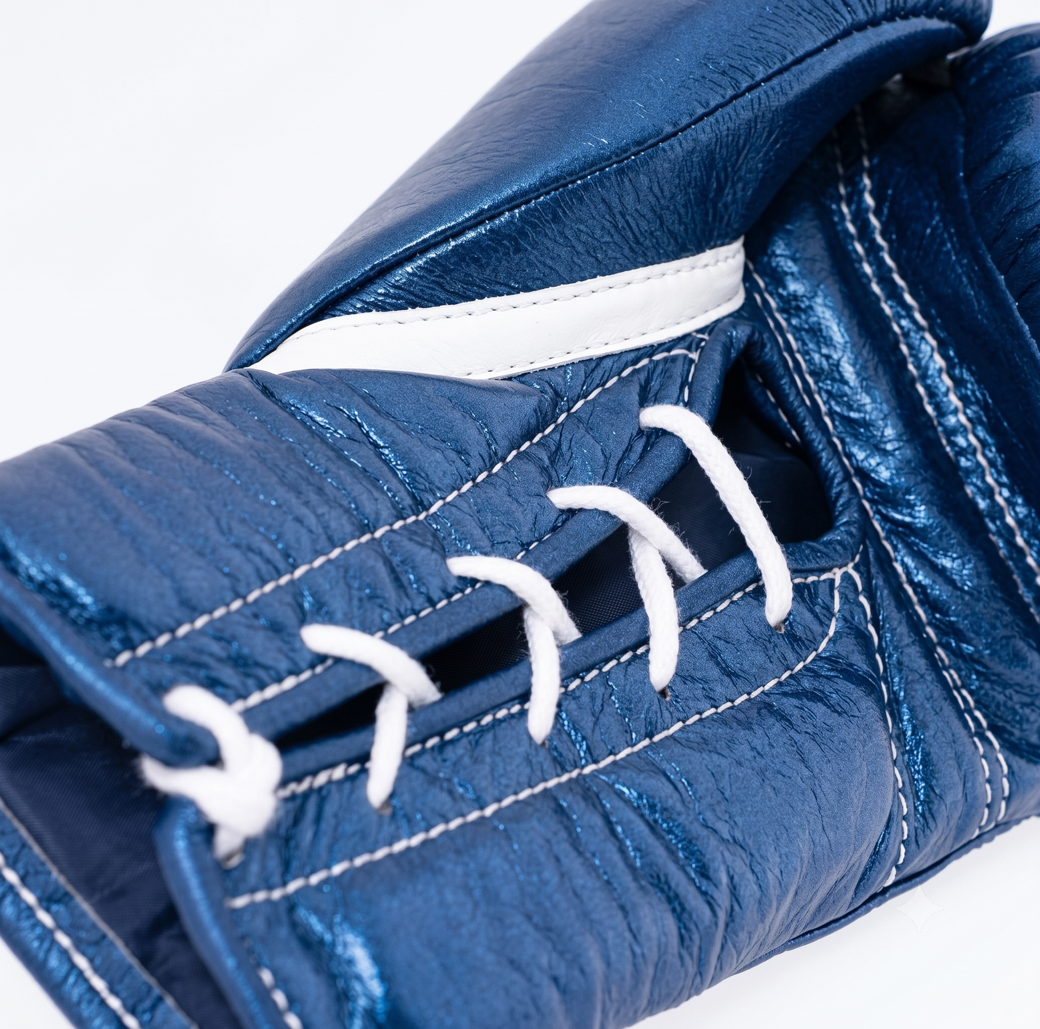 A close-up of a blue leather boxing glove showing the textured leather, white contrast stitching, and white laces against a white background.