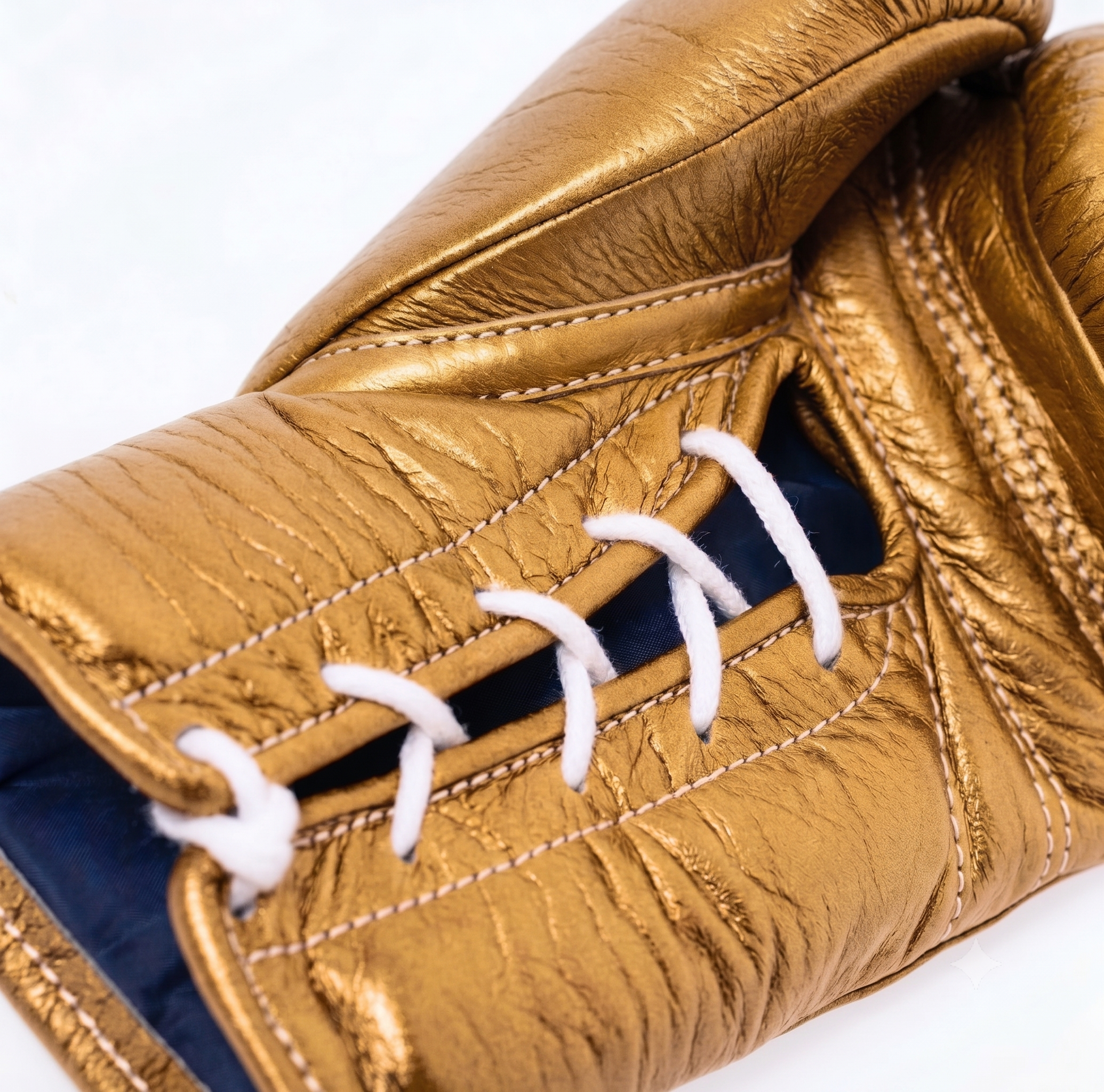 Close-up of a metallic gold boxing glove with white laces and contrast stitching, showing the textured leather and inner blue lining.