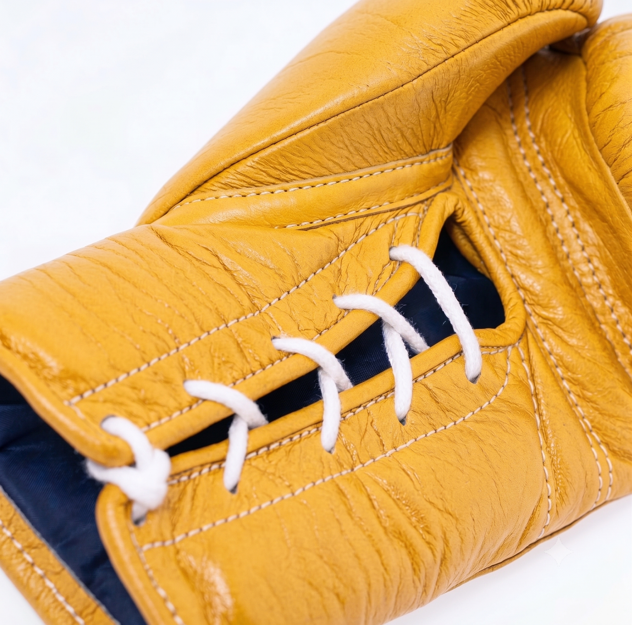 Close-up of a mustard yellow leather boxing glove with white laces and contrast stitching, showing a dark blue interior lining.