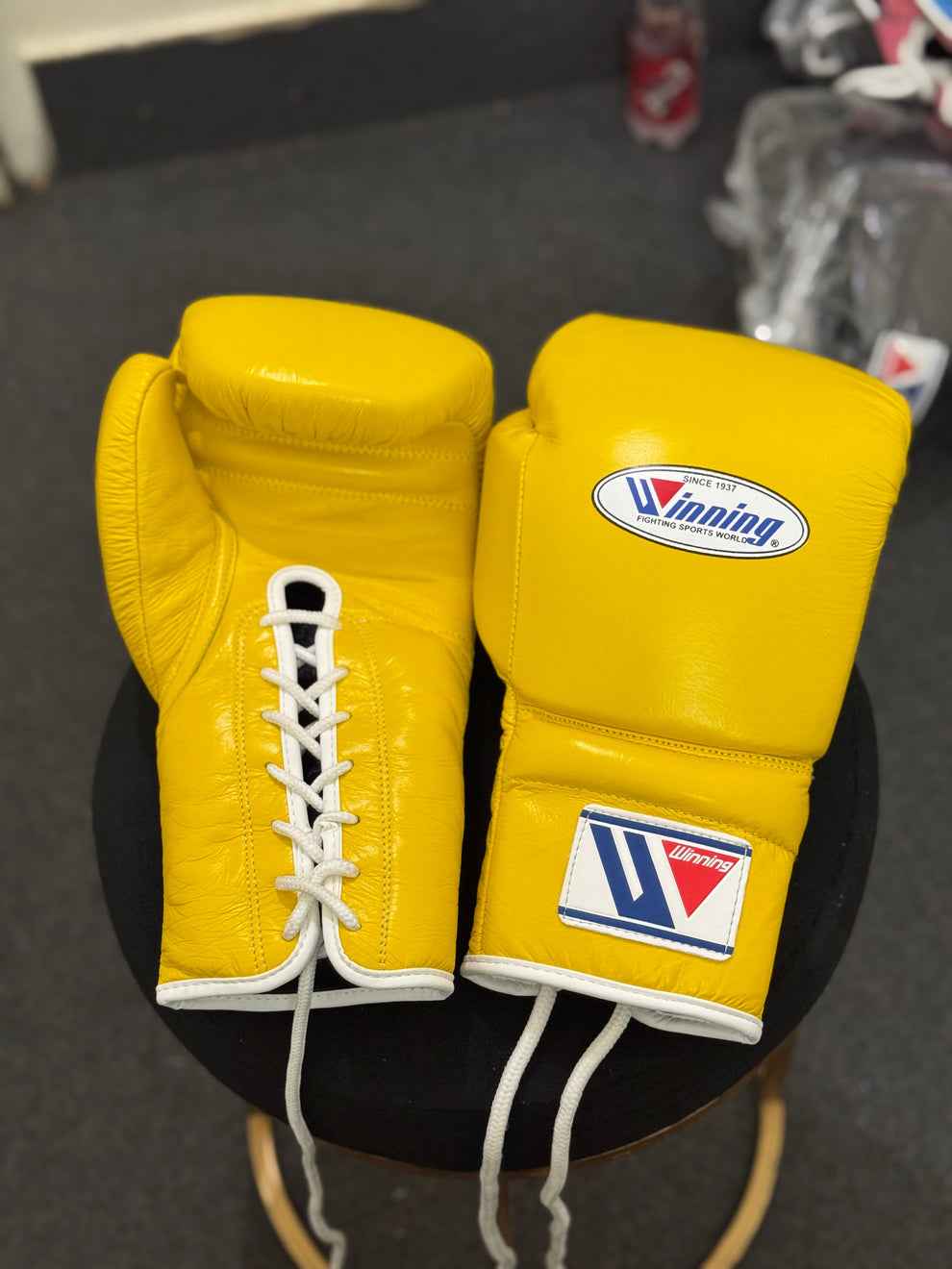 Winning professional lace-up boxing gloves in vibrant yellow leather with official white branding patches and white laces resting on a stool.