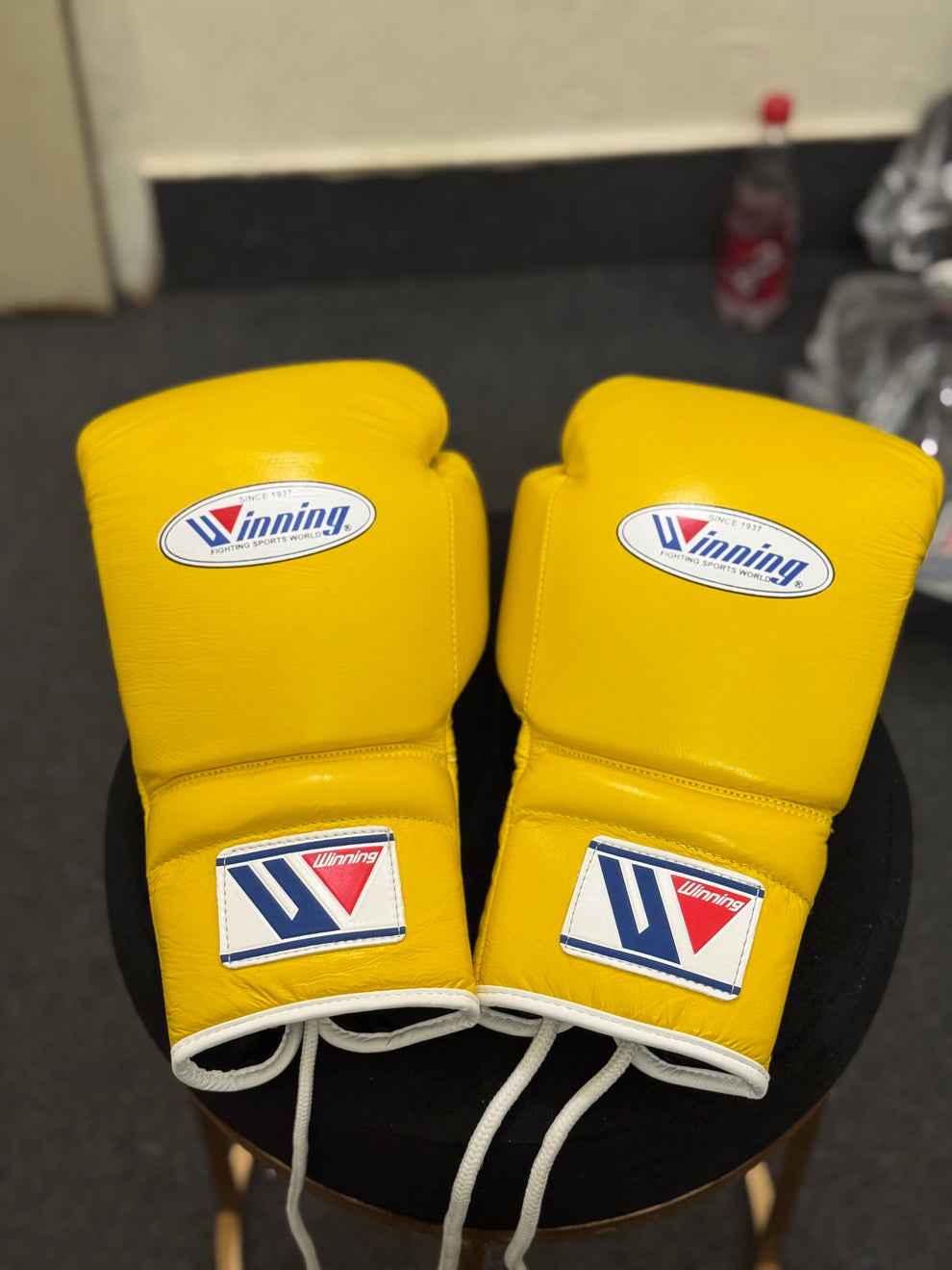 Winning professional lace-up boxing gloves in vibrant yellow leather with official white branding patches and white laces resting on a stool.