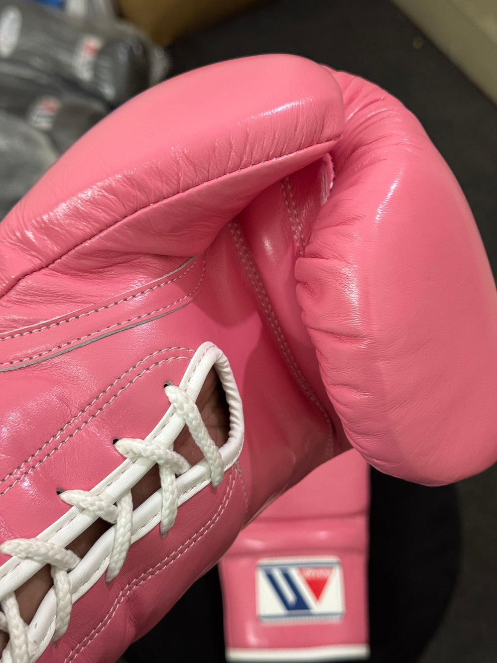 Official Winning professional lace-up training boxing gloves in premium pink leather resting on a dark stool, featuring white laces, white contrast edge trim, and the iconic brand logo crest on the cuffs.