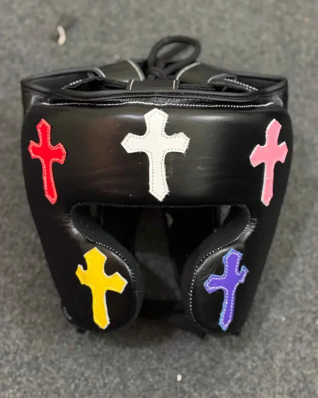 Custom black leather boxing headgear with multi-colored cross patches and professional lace-top closure.