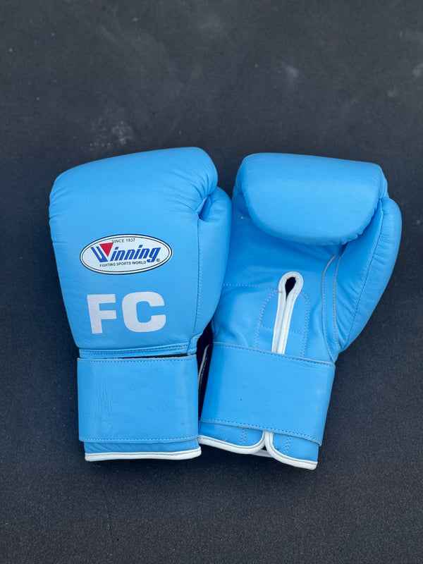 Custom Winning professional hook-and-loop training boxing gloves in premium sky blue leather featuring white edge piping and a white FC initial logo printed on the knuckle face.