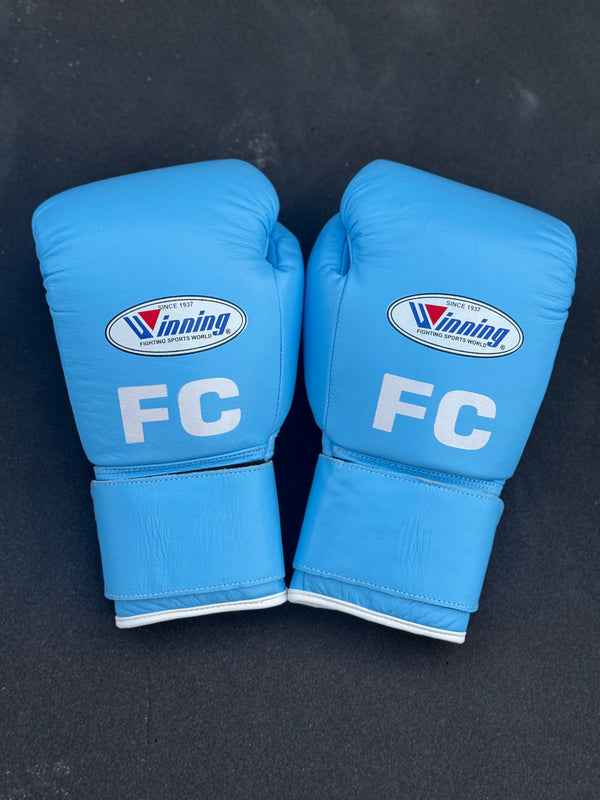 Custom Winning professional hook-and-loop training boxing gloves in premium sky blue leather featuring white edge piping and a white FC initial logo printed on the knuckle face.
