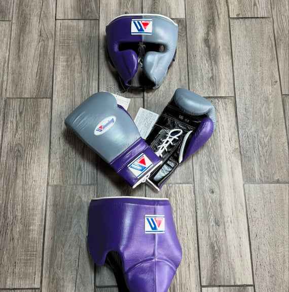 Custom Winning professional 3-piece boxing sparring gear set in a matching metallic gray and purple premium leather colorway, featuring 16 oz lace-up gloves, a split-face headgear, and a purple groin protector arranged on a gray wood floor.