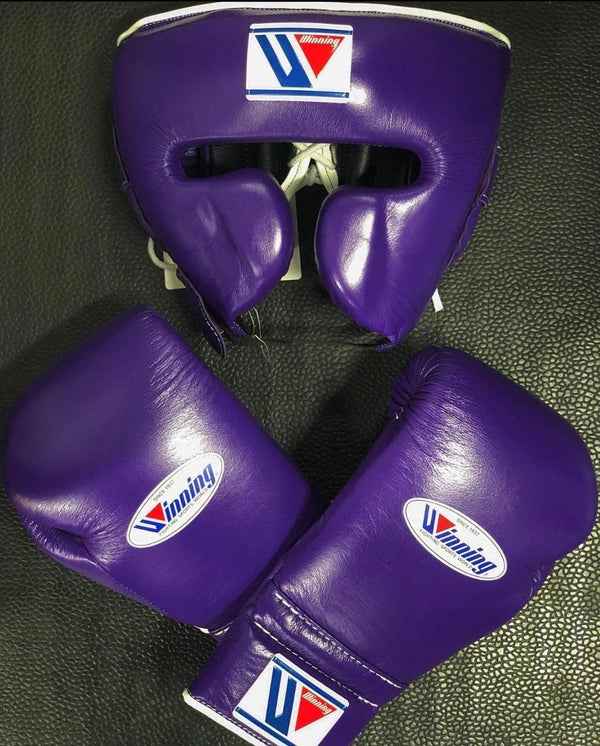 Official Winning professional boxing sparring set in a matching classic purple premium leather colorway, featuring lace-up training gloves and a face guard headgear over a textured dark backdrop.