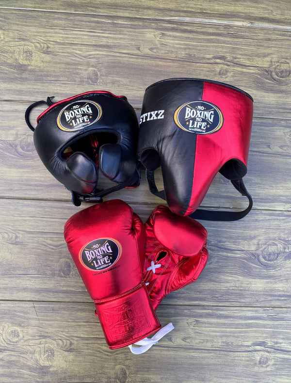 Official No Boxing No Life professional boxing sparring set featuring metallic red lace-up gloves, a black cheek protection headgear, and a matching black and metallic red split split-face face bar headgear on a wooden background.