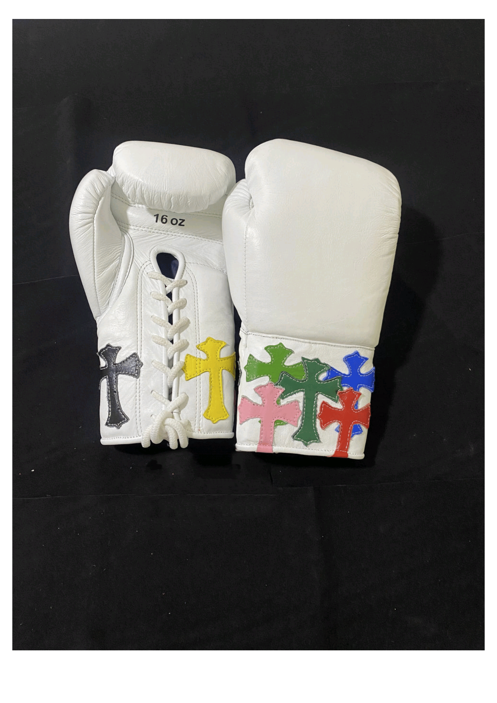 Custom white leather lace-up training boxing gloves featuring vibrant multi-colored stitched cross patches on the cuffs and a traditional white lacing system against a black backdrop.