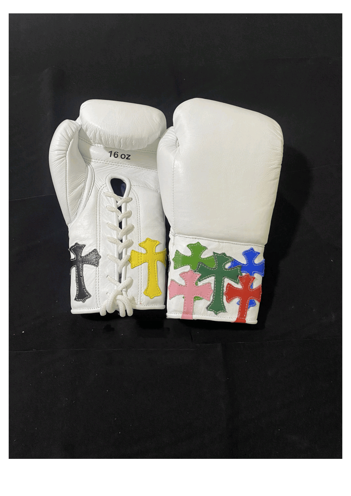Custom white leather lace-up training boxing gloves featuring vibrant multi-colored stitched cross patches on the cuffs and a traditional white lacing system against a black backdrop.