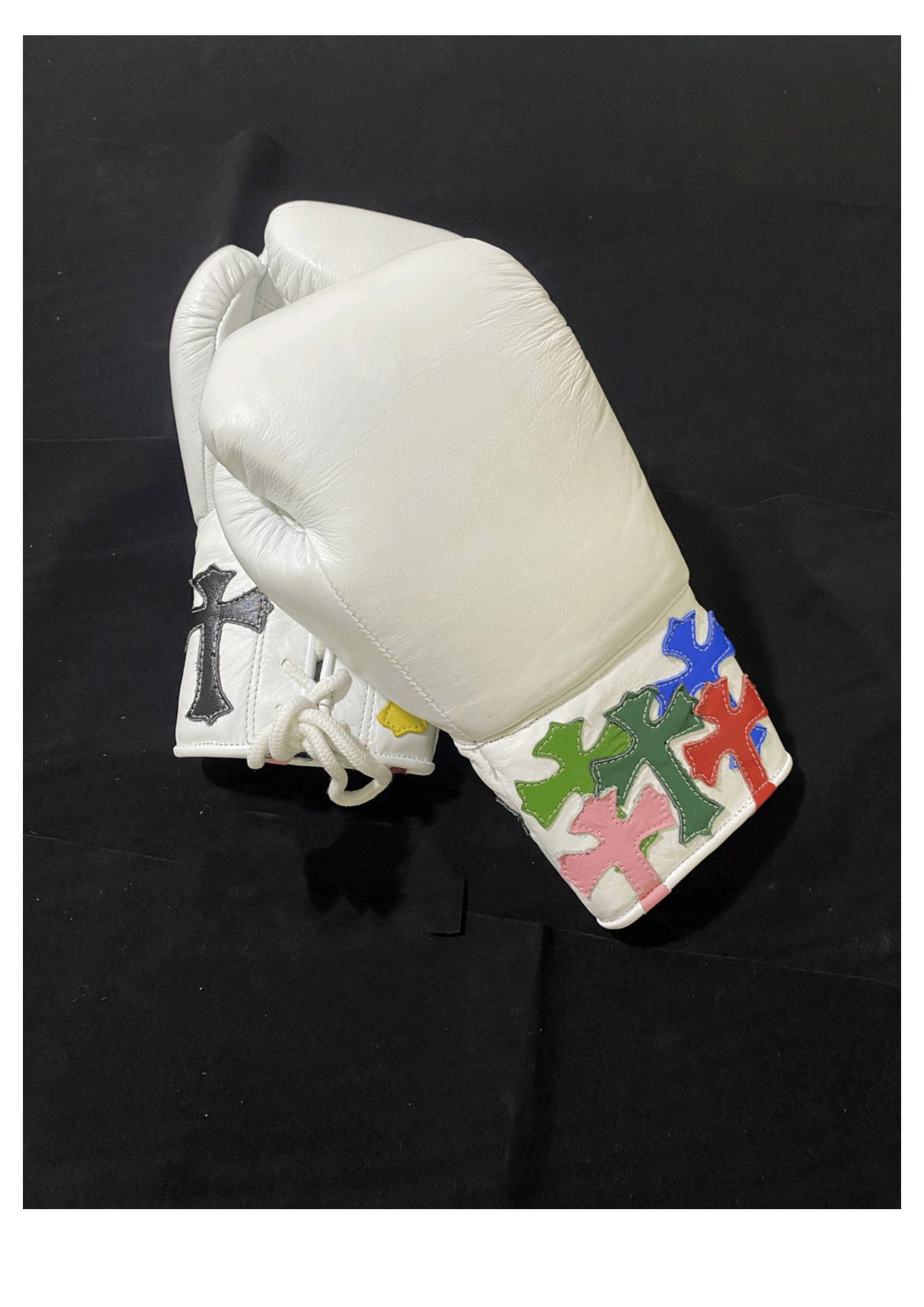 Custom white leather lace-up training boxing gloves featuring vibrant multi-colored stitched cross patches on the cuffs and a traditional white lacing system against a black backdrop.