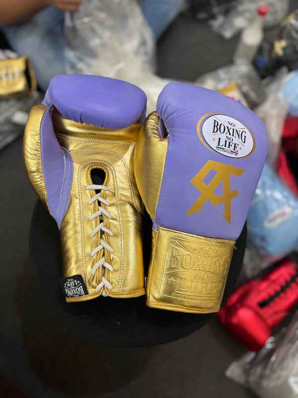 Official No Boxing No Life professional lace-up boxing gloves in premium lavender and metallic gold leather featuring a gold Canelo Alvarez CA logo printed below the brand insignia.