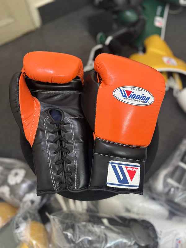 Custom Winning professional lace-up training boxing gloves in a vibrant orange and black leather colorway featuring the iconic brand logo patches on the knuckles and cuffs.