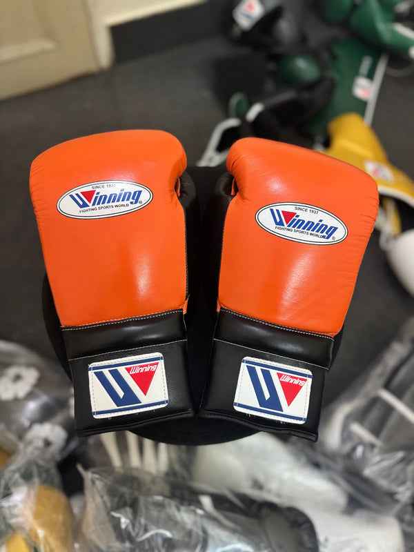 Custom Winning professional lace-up training boxing gloves in a vibrant orange and black leather colorway featuring the iconic brand logo patches on the knuckles and cuffs.