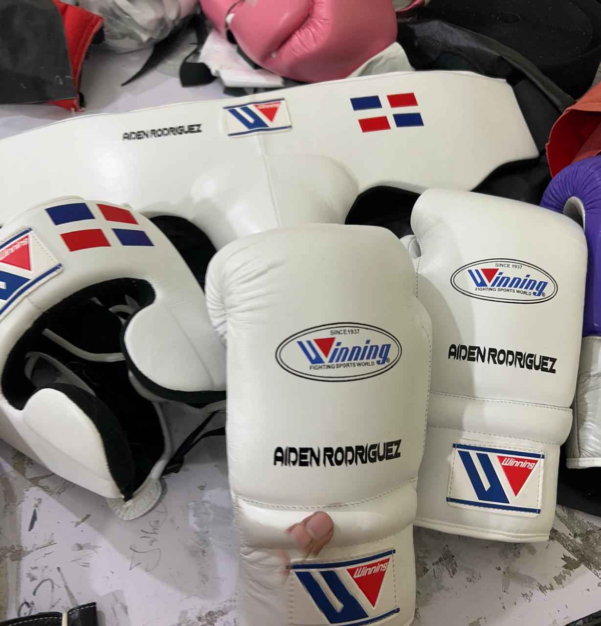 Official Winning professional lace-up training boxing gloves in pristine white premium leather resting on a wooden surface, featuring the iconic brand logo oval crest on the knuckle face and cuff patches.